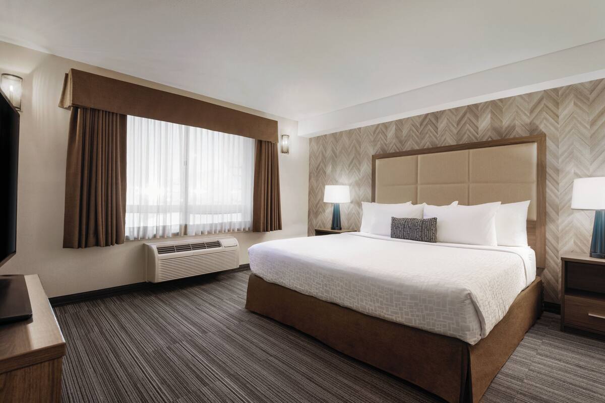 A hotel room with a large bed, a flat-screen TV, a desk, and a window with curtains.