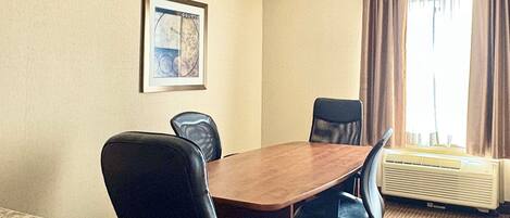 A conference room with a wooden table, four black office chairs, a framed picture on the wall, and a window with curtains.