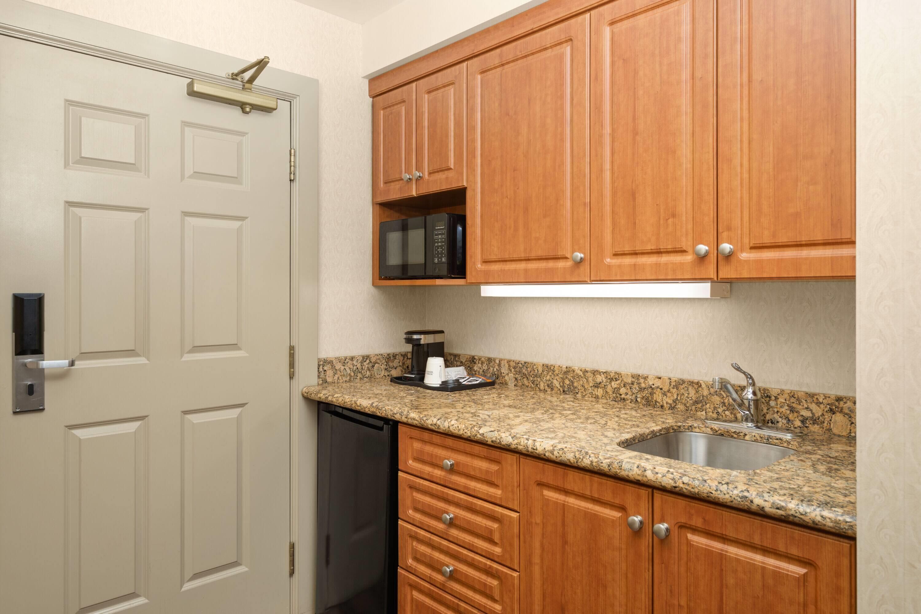 A compact kitchen with wooden cabinets, a granite countertop, a built-in microwave, and a dishwasher.