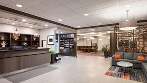 A hotel lobby with a reception desk, a pantry, a seating area with a sofa and coffee table, and a decorative wall. - Waterloo Suites Hotel, Trademark Collection by Wyndham (Waterloo)