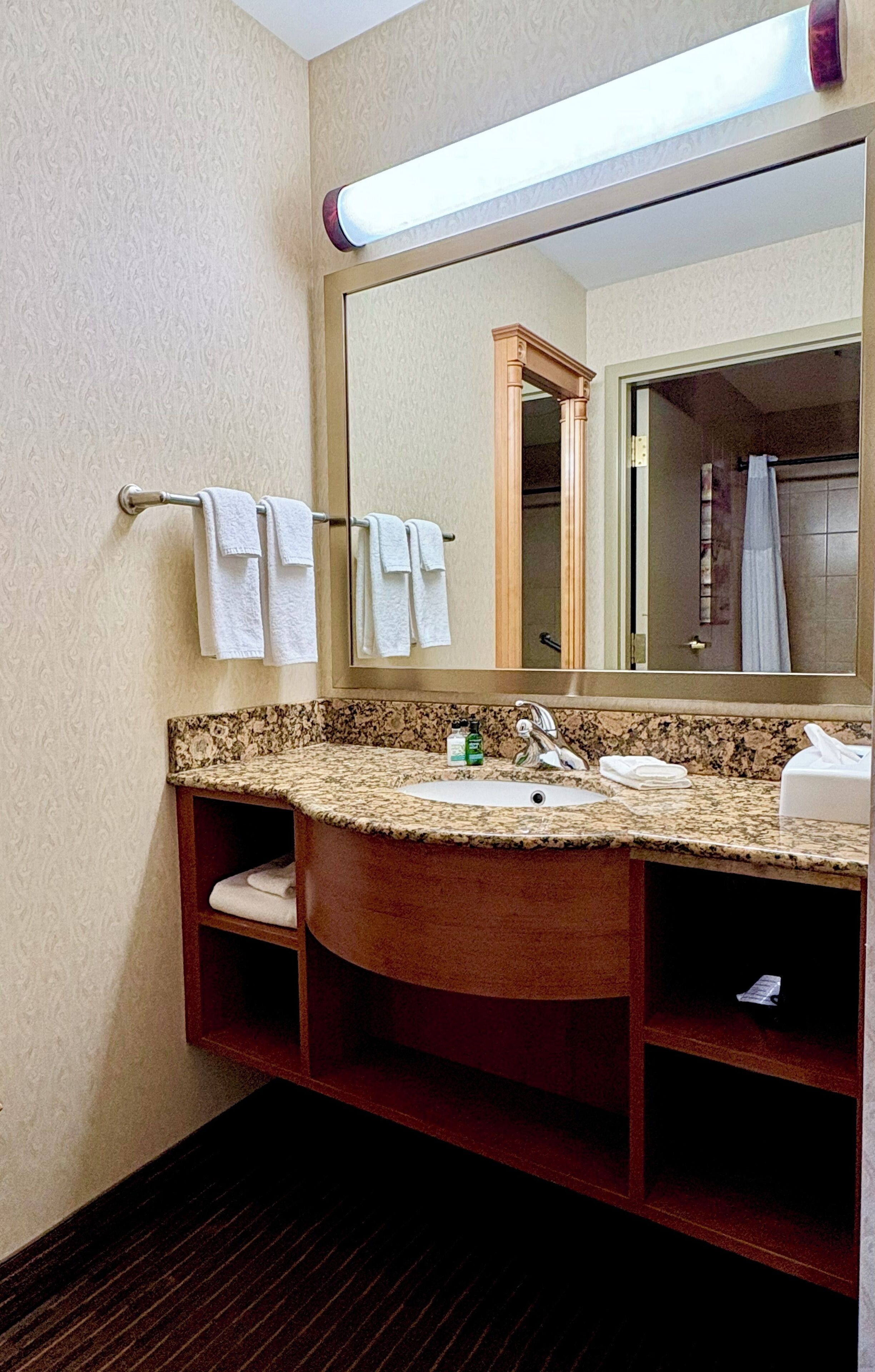 A bathroom with a marble sink, wooden vanity, and a large mirror.