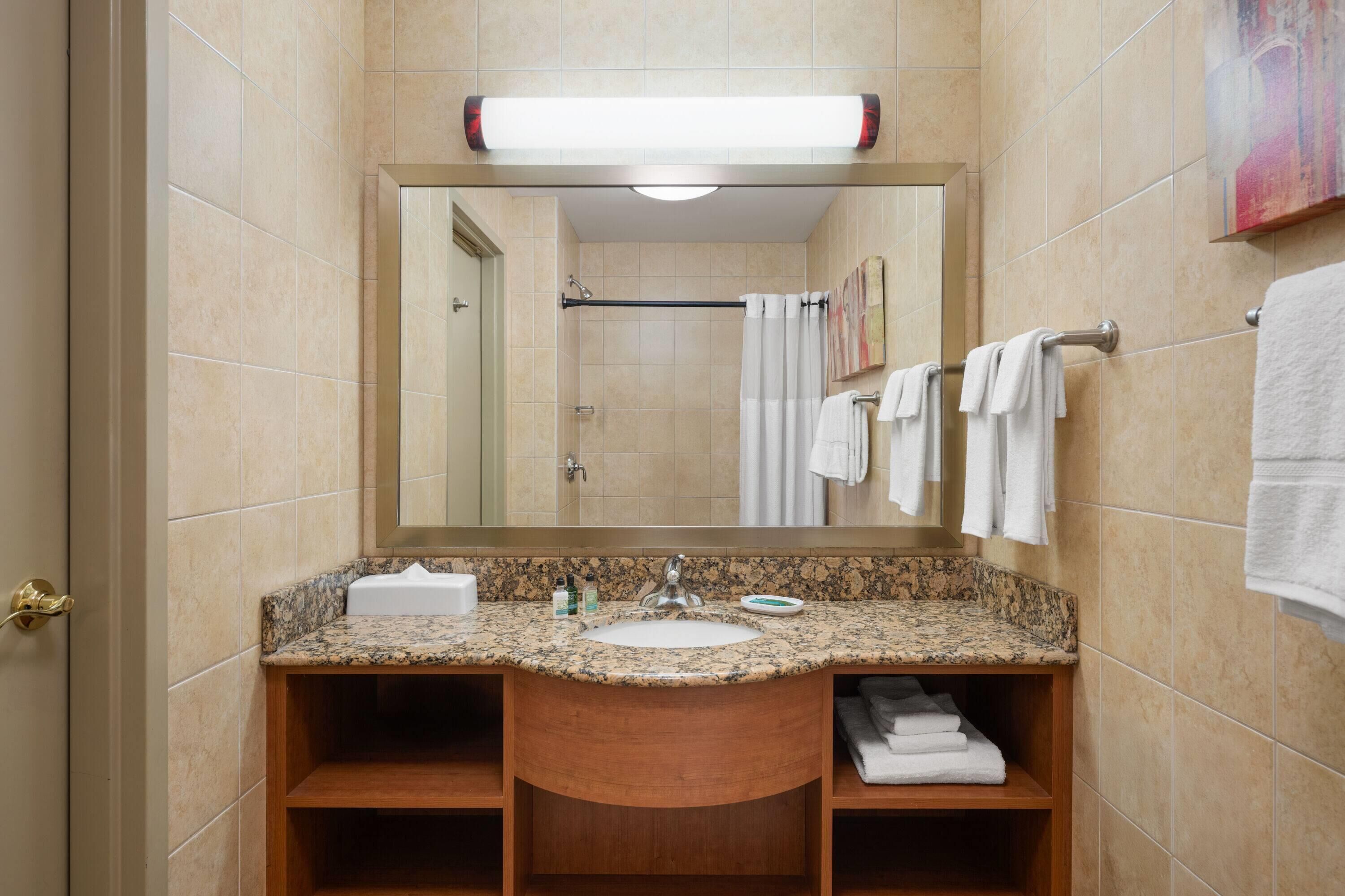 A bathroom with a granite countertop sink, a mirror, and a towel rack.