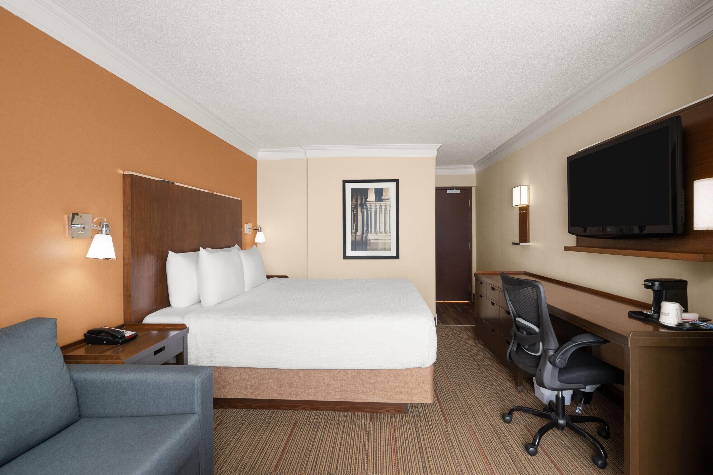 A hotel room with a large bed, a desk with a chair, a television, and a coffee maker.