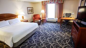 A hotel room with a large bed, a desk, a chair, a television, and a window with curtains.