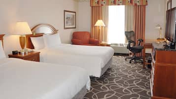 A hotel room with two beds, a desk, a chair, a TV, and a window with curtains.