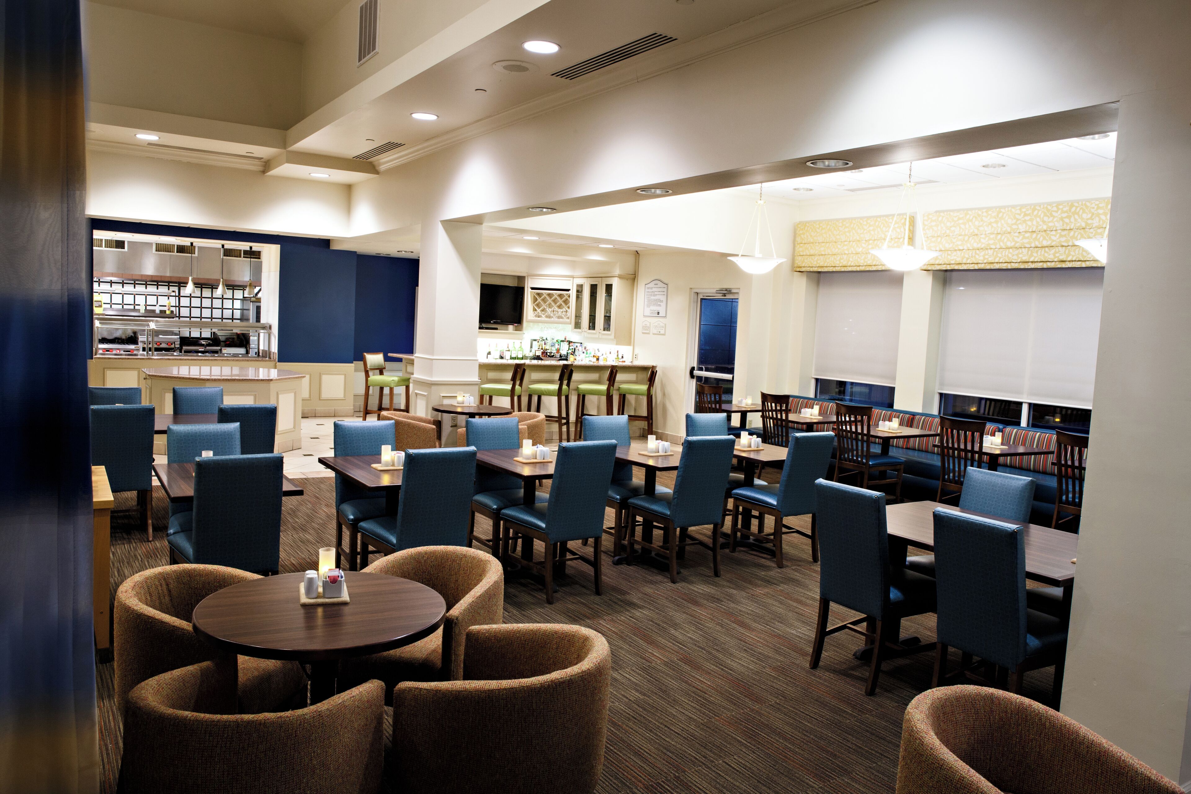 Un restaurante de hotel con varias zonas de estar, incluyendo mesas redondas y cabinas, y una barra visible al fondo.