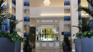 Un hall d’hôtel avec un comptoir d’accueil, des plantes en pot et un sol carrelé.