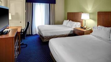 A hotel room with two beds, a desk with a TV, a lamp, and a telephone.