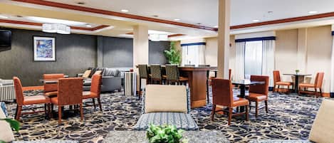 A hotel lobby with a seating area, a reception desk, and a television on the wall.