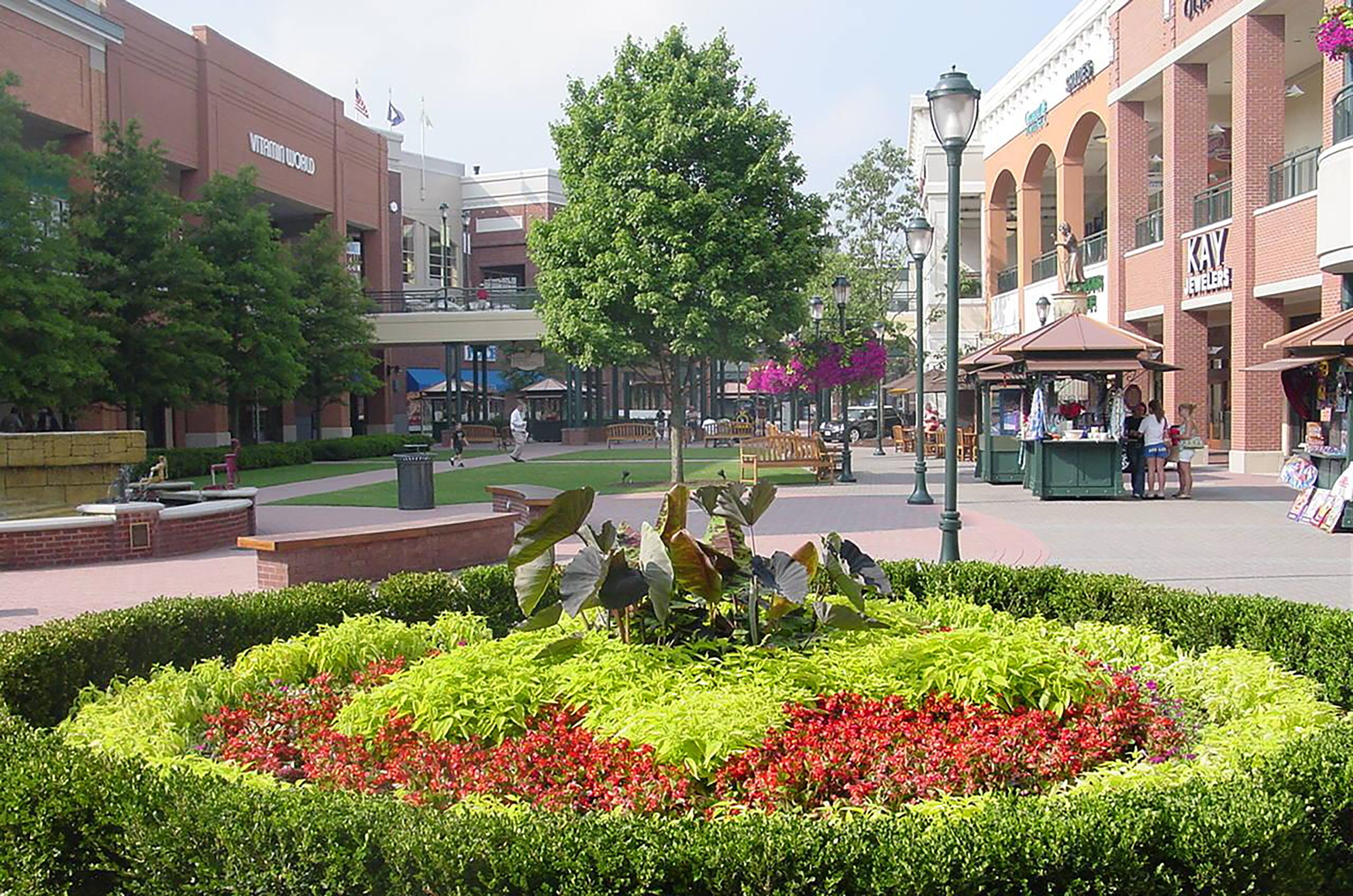 A public square with a central garden, benches, and a kiosk.