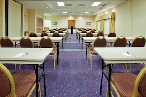 Un salón de conferencias con mesas y sillas dispuestas en filas, suelo alfombrado y un atril al frente.