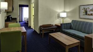 A hotel room with a sofa, a small table, a chair, a lamp, and a painting on the wall.