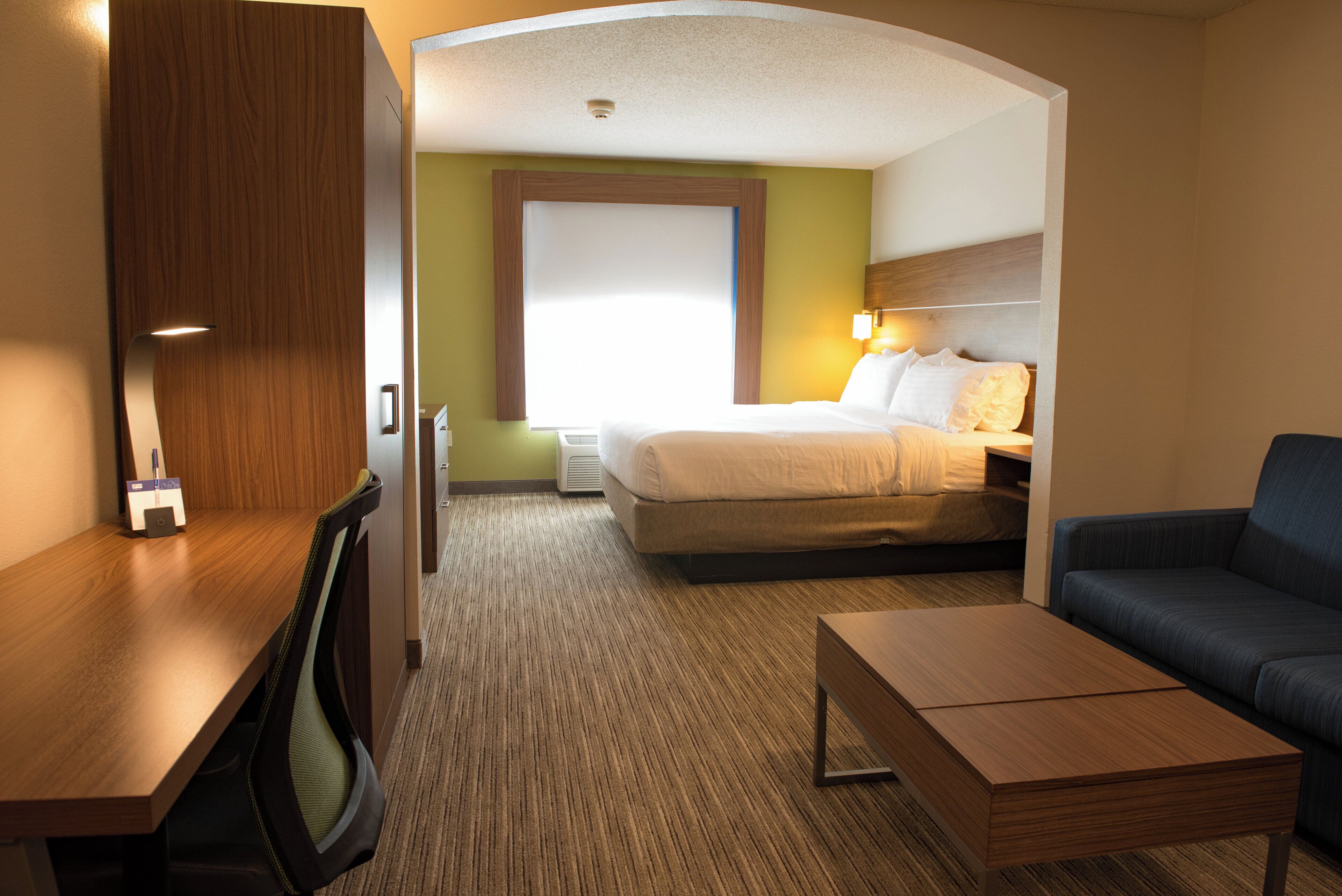 A hotel room with a bed, a desk, a chair, and a sofa.
