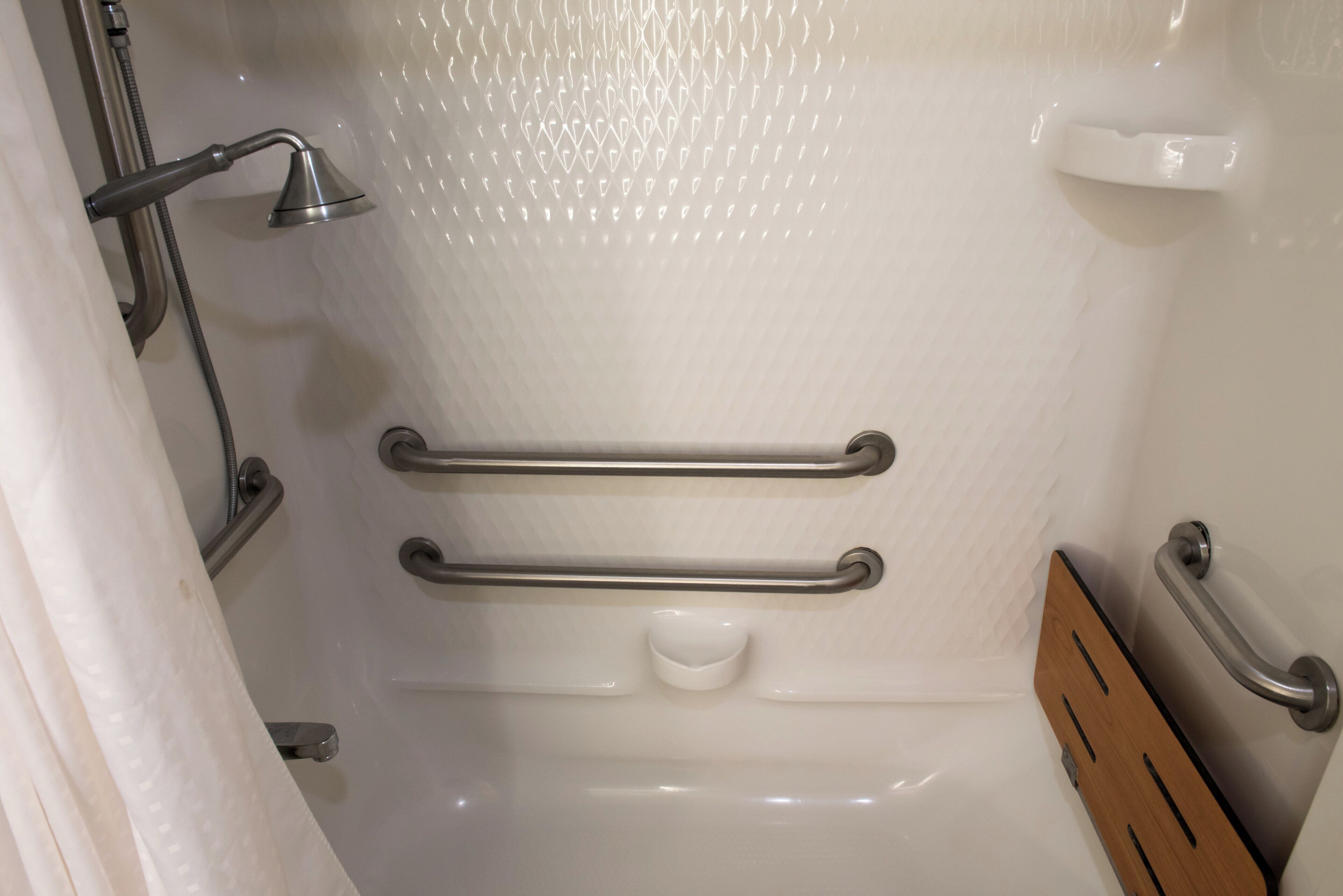 Een badkamer met douche, handgrepen en een houten paneel.
