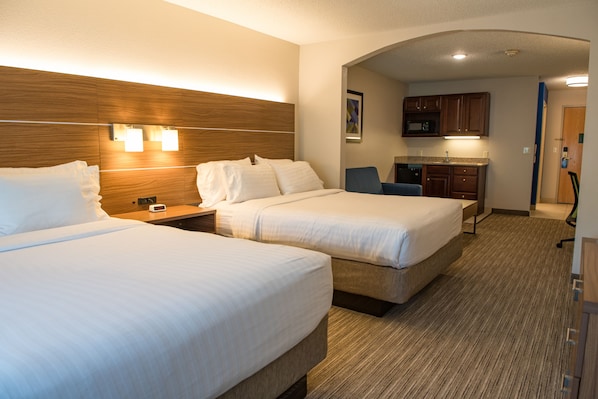 A hotel room with two beds, a nightstand, a desk, and a kitchenette.