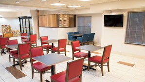 Un restaurant avec des chaises et des tables rouges, un espace buffet et un téléviseur fixé au mur.
