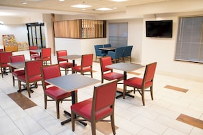 Un restaurant avec des chaises et des tables rouges, un espace buffet et un téléviseur fixé au mur.