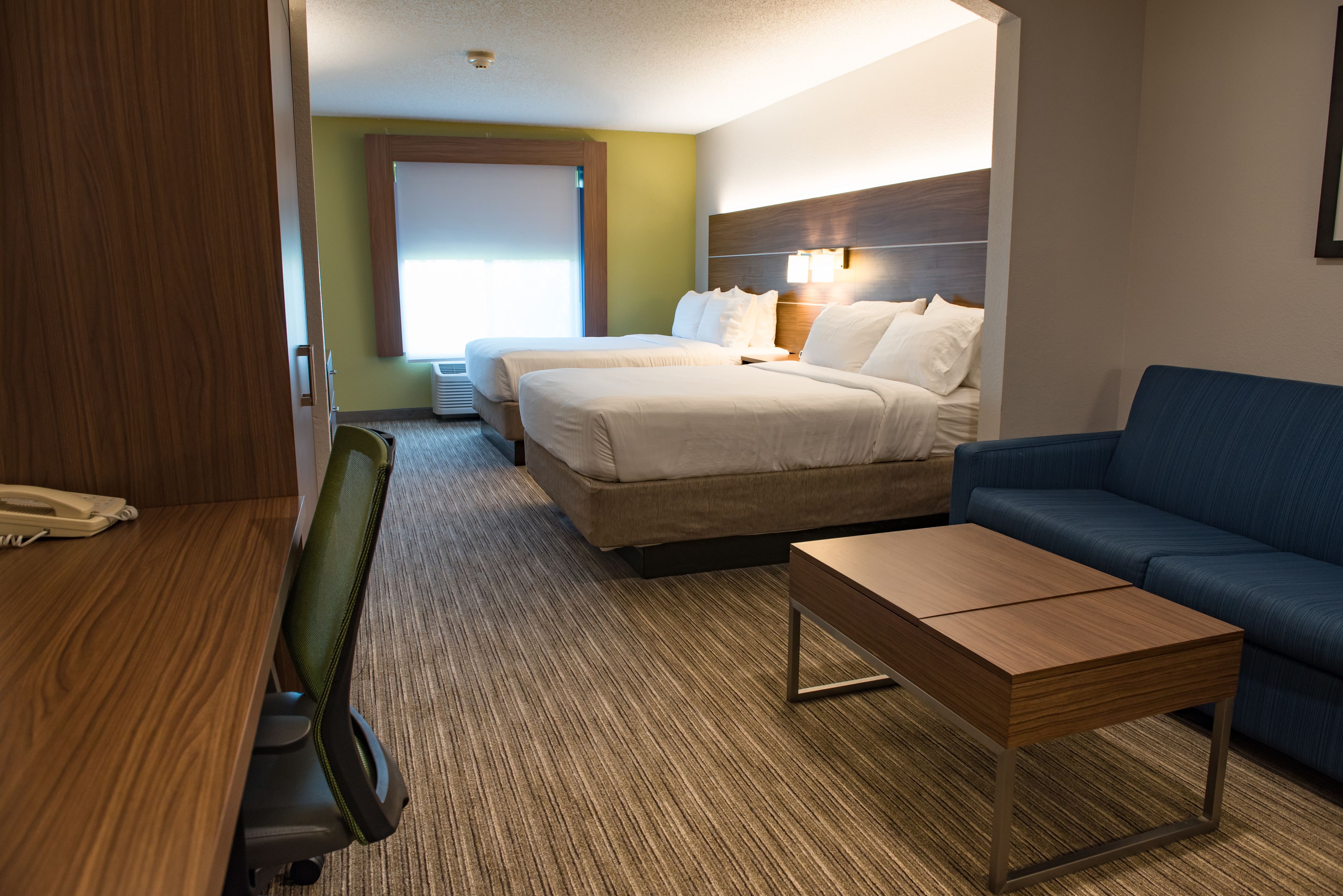 A hotel room with two beds, a blue sofa, a wooden coffee table, and a desk with a chair.