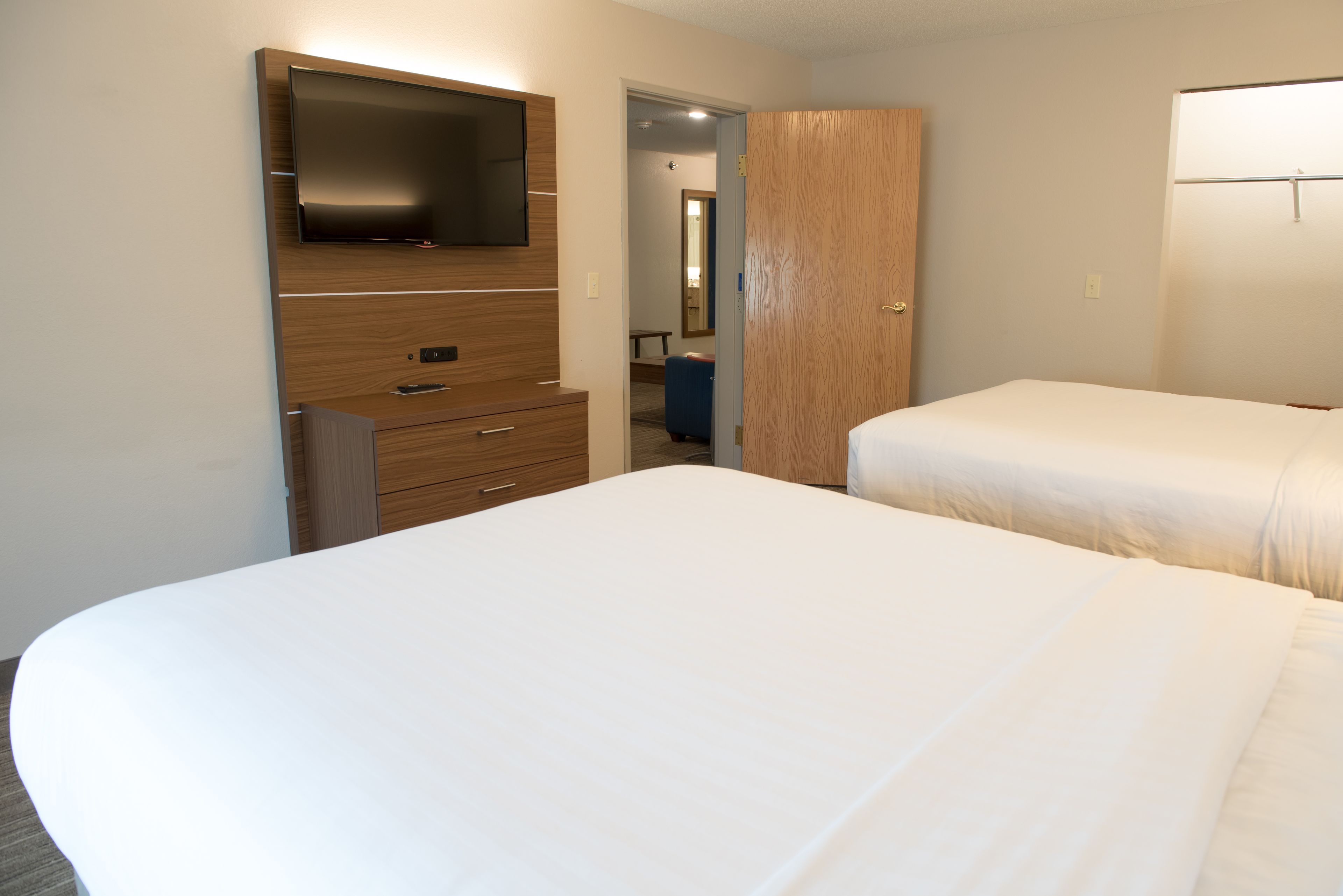 A hotel room with a large bed, a wooden dresser with a flat-screen TV, and a wardrobe.