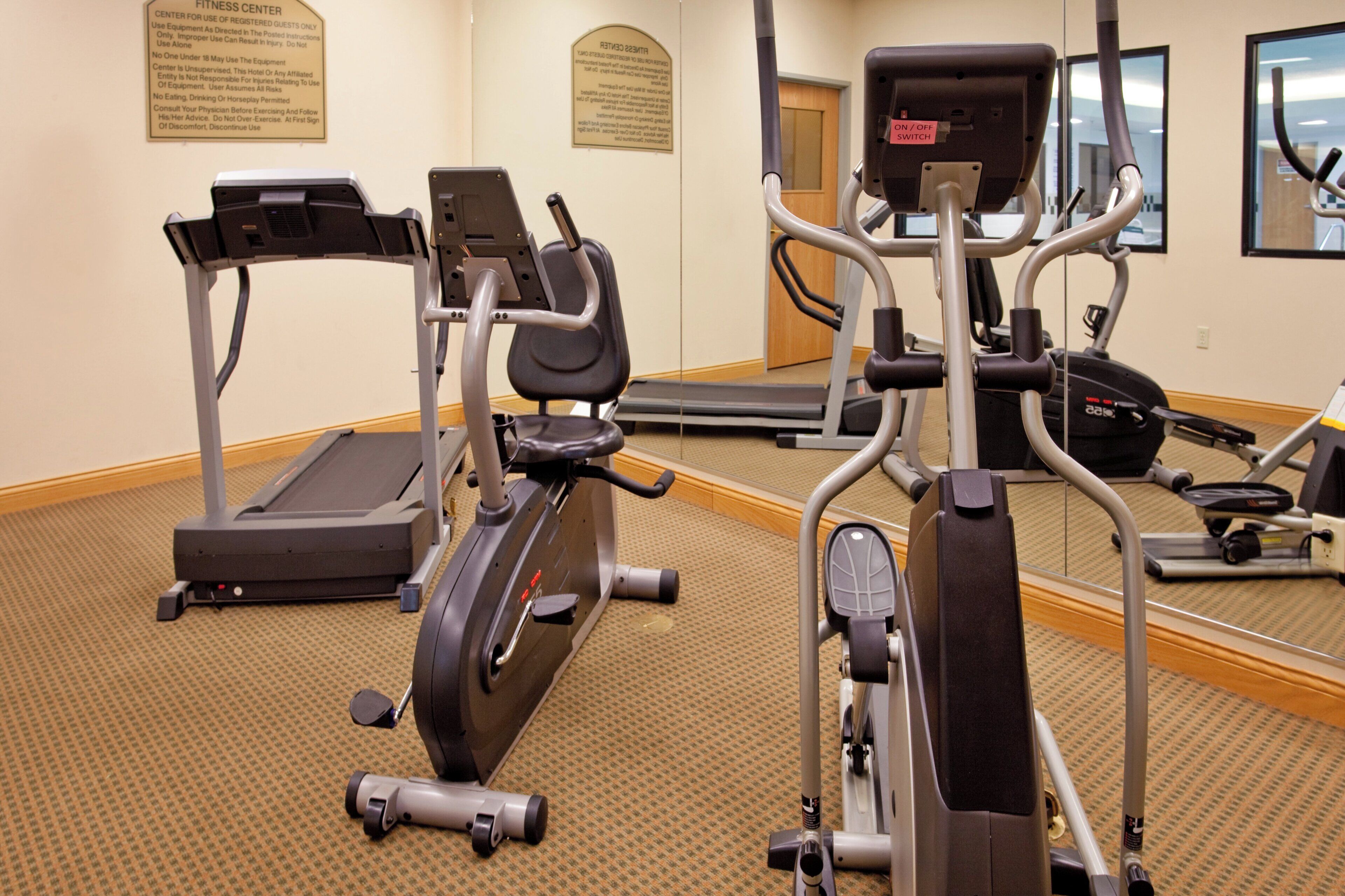 A fitness center with treadmills, elliptical machines, and a mirrored wall.