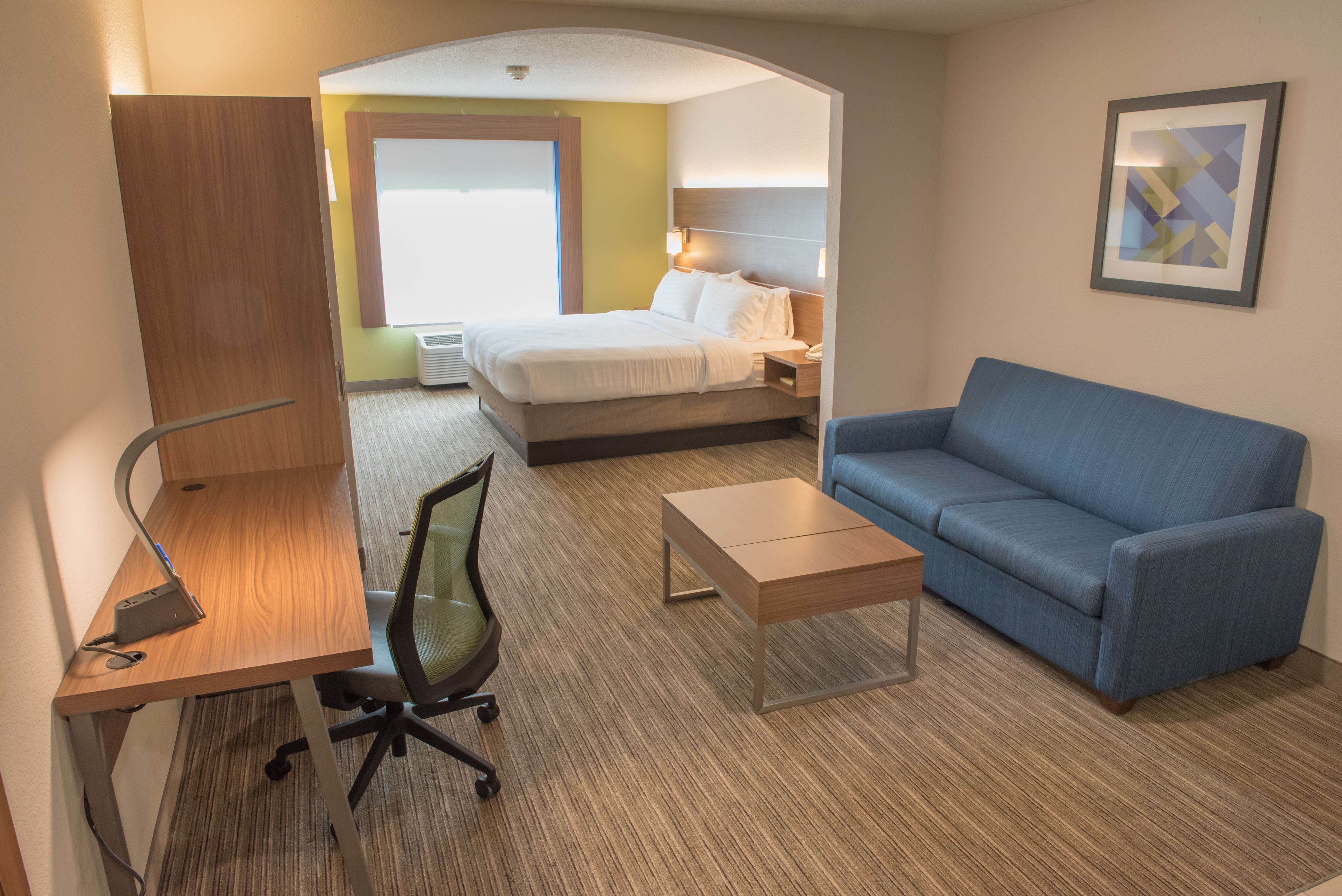 A hotel room with a bed, a blue sofa, a desk with a computer, and a chair.