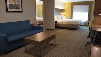 A hotel room with a blue sofa, a wooden coffee table, a bed with white bedding, and a desk with a chair.