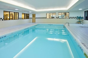 Une piscine intérieure à l’eau claire, avec des murs et un sol carrelés.