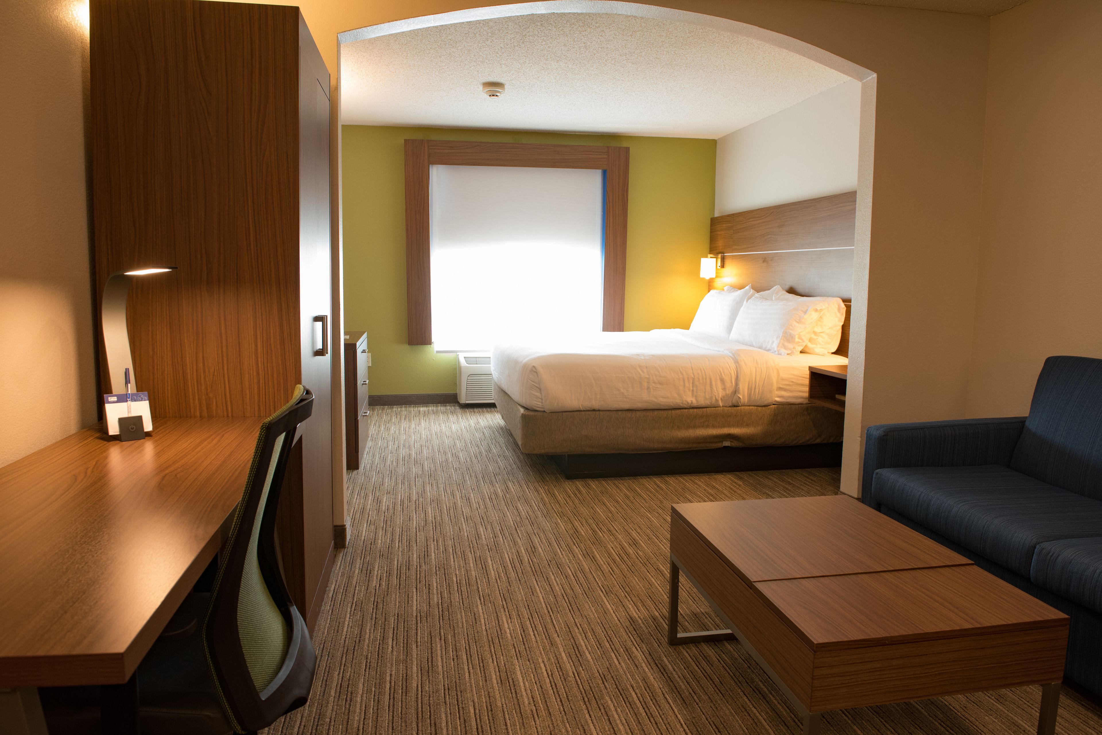 A hotel room with a bed, a desk, a chair, a sofa, and a carpeted floor.