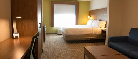 A hotel room with a bed, a desk, a chair, a sofa, and a carpeted floor.