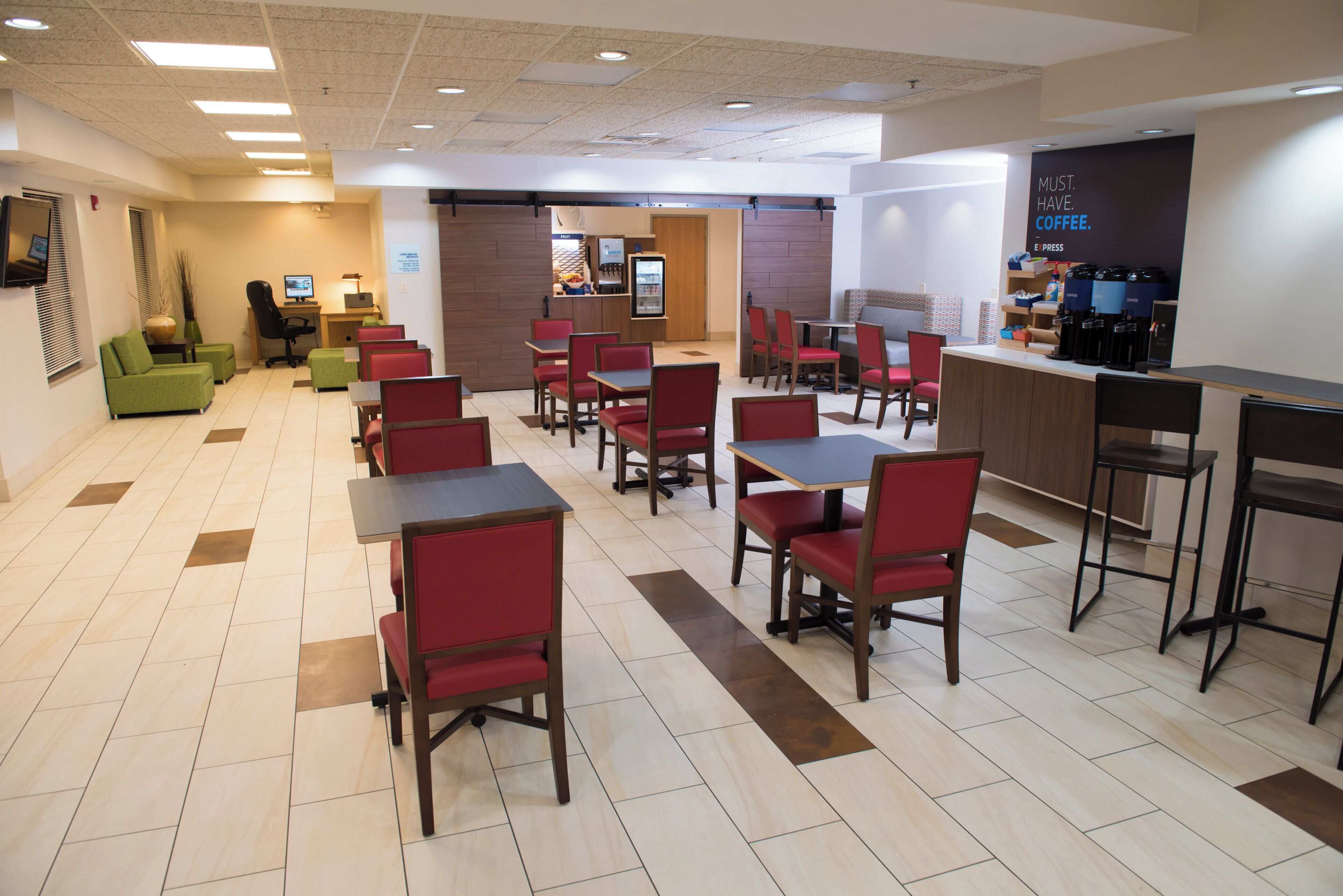 A hotel dining area with multiple tables and chairs, a coffee station, and a fruit bar.