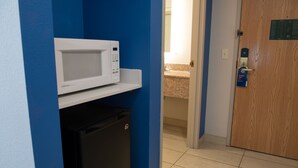 A compact kitchen area with a microwave on a white shelf, a black refrigerator, and a wooden door with a sign. - Holiday Inn Express & Suites Elkhart by IHG (Elkhart)