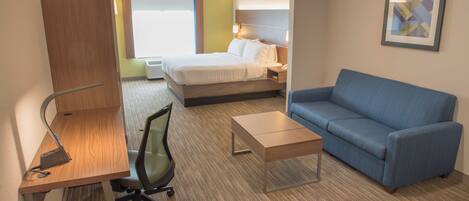 A hotel room with a bed, a blue sofa, a desk with a chair, and a small table.