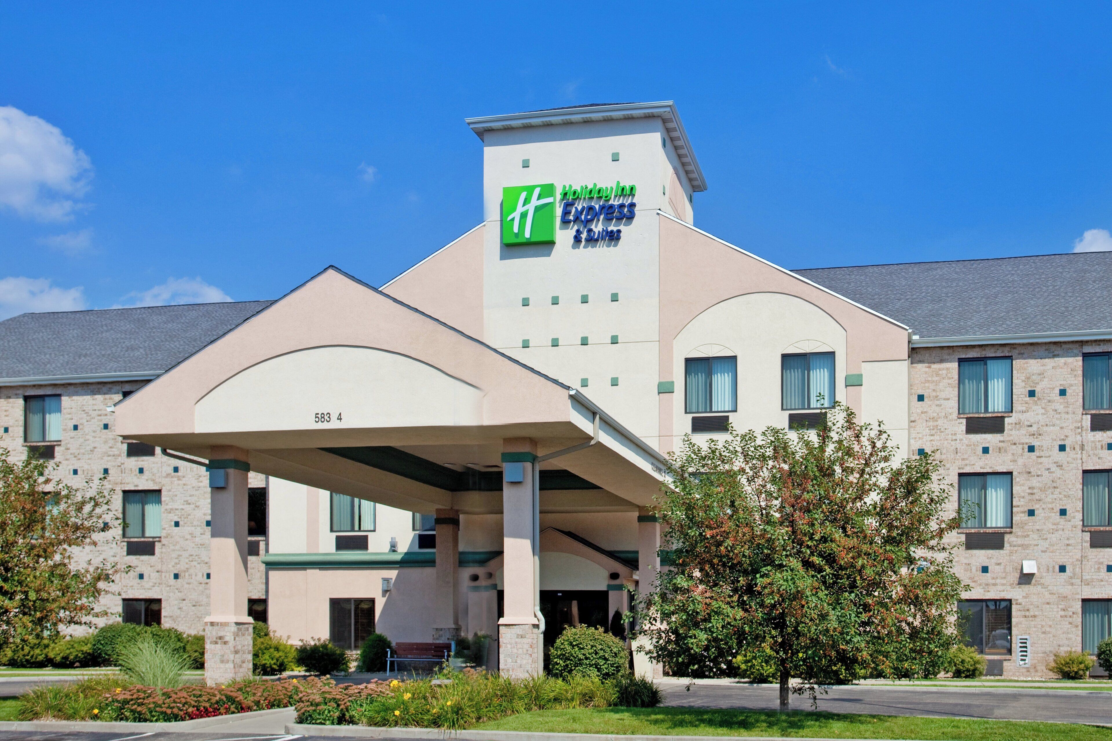 En byggnad som inrymmer ett Holiday Inn Express & Suites-hotell, med en ingång som är skyddad av ett tak och en fasad av tegel.