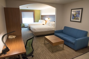 A hotel room with a bed, a blue sofa, a desk with a lamp, and a small table.
