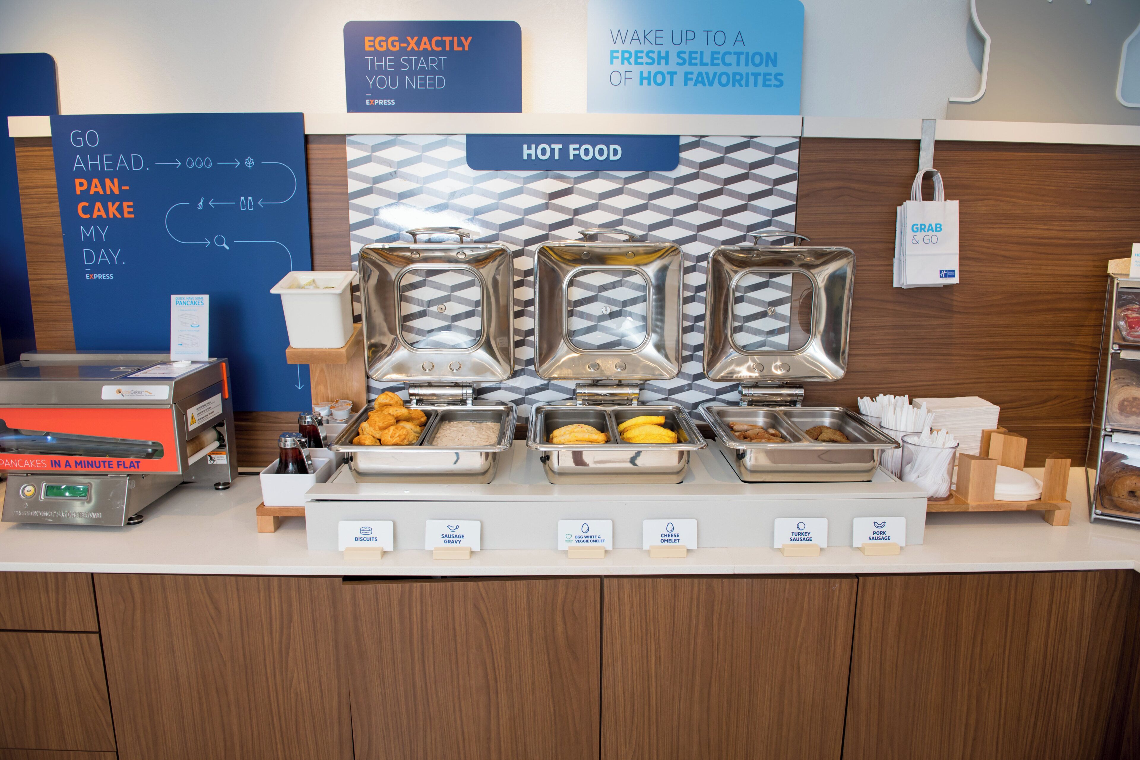 A breakfast buffet with labeled food stations including pancakes, sausages, and eggs.