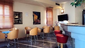 Habitación de hotel con zona de bar, asientos, televisor y un cuadro en la pared.
