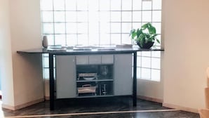 Una habitación con suelo de mármol, una mesa negra con cajones y un amplio ventanal con persianas.