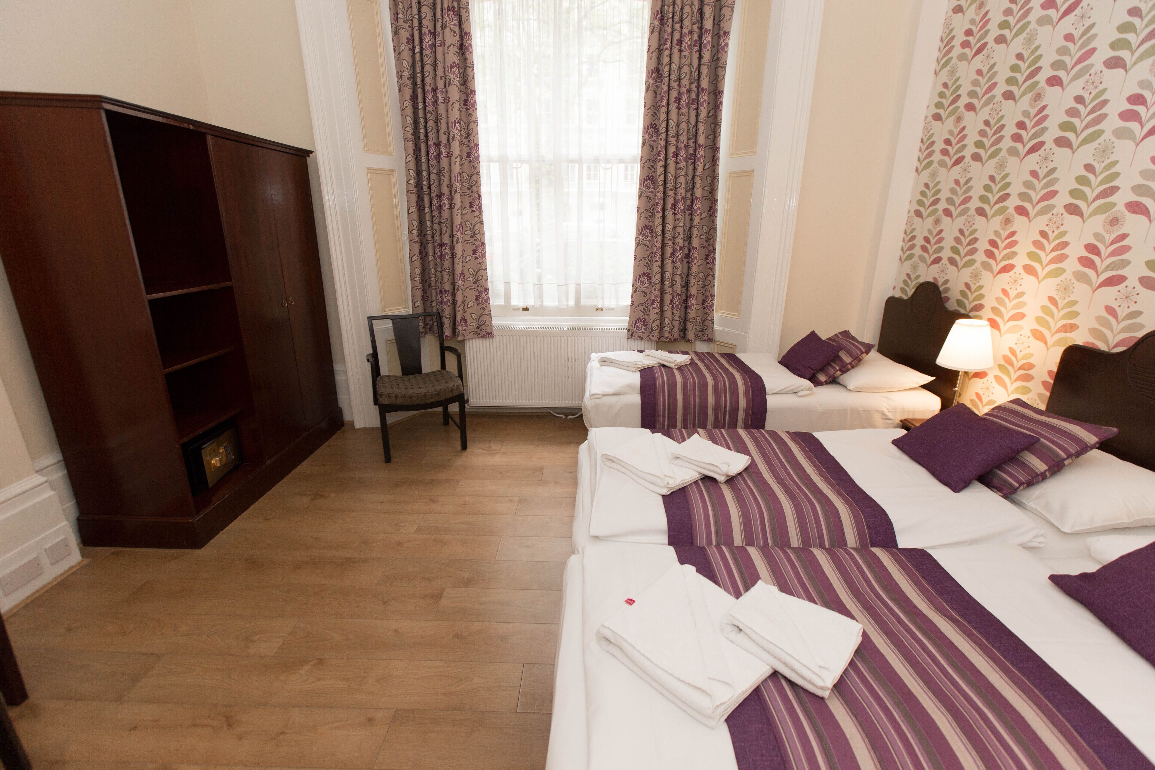 A hotel room with two beds, a wardrobe, a radiator, and a window with curtains.