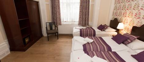 A hotel room with two beds, a wardrobe, a radiator, and a window with curtains.