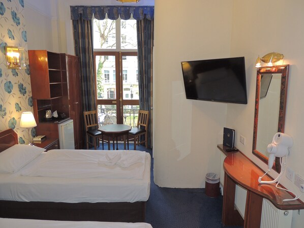 Une chambre d’hôtel avec un lit, un bureau doté d’un miroir, une télévision et une fenêtre avec des rideaux.
