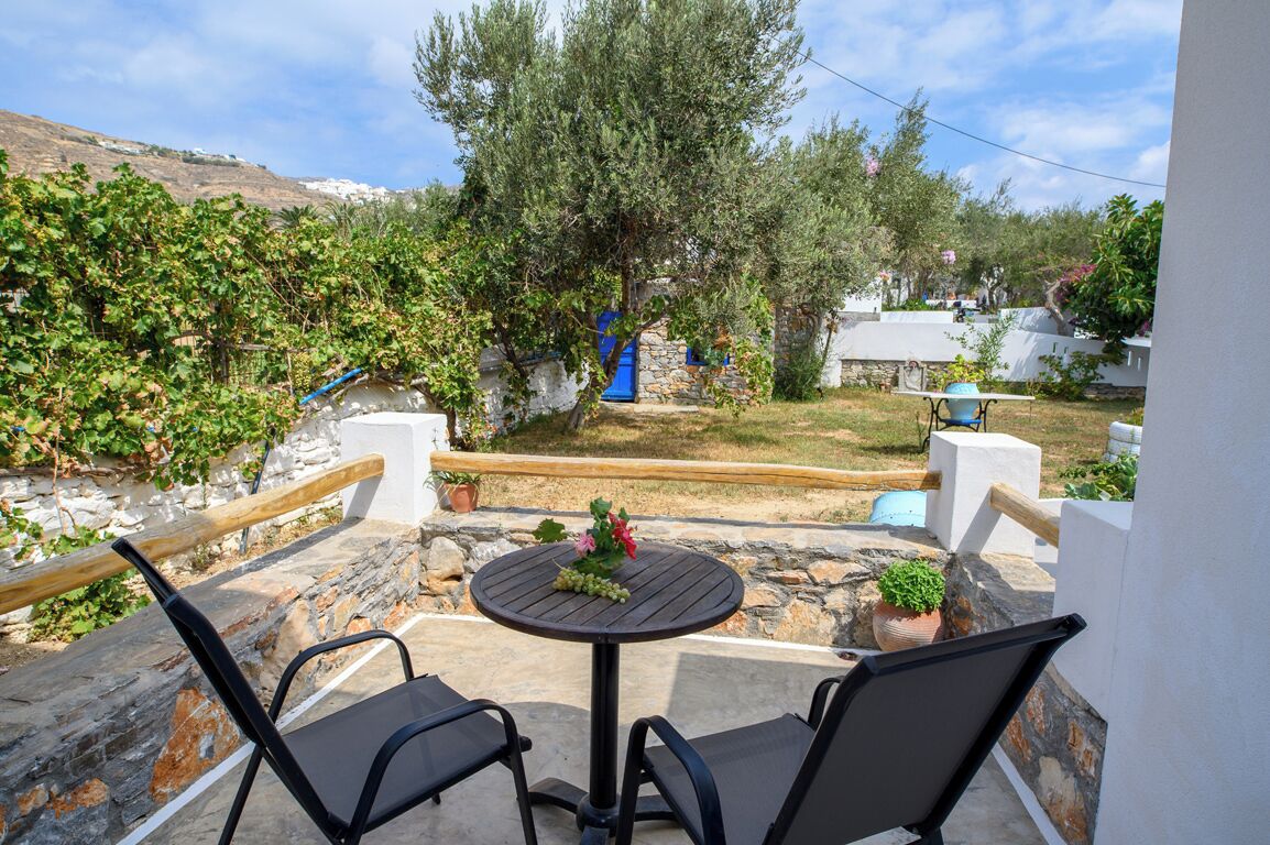Un patio con una mesa redonda y dos sillas, con vistas a un jardín con árboles y un muro de piedra.