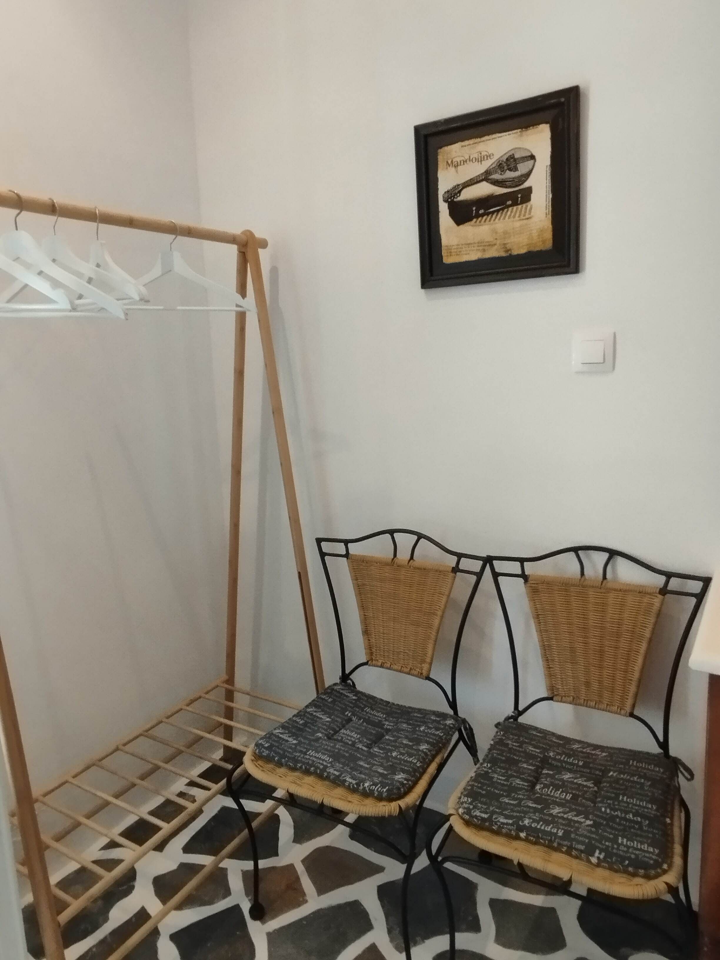 Un área de lavandería con un tendedero de madera, dos sillas de mimbre con cojines y un cuadro en la pared.