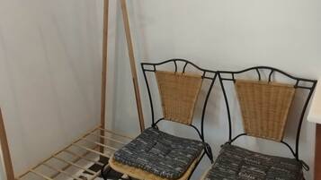 Un área de lavandería con un tendedero de madera, dos sillas de mimbre con cojines y un cuadro en la pared.