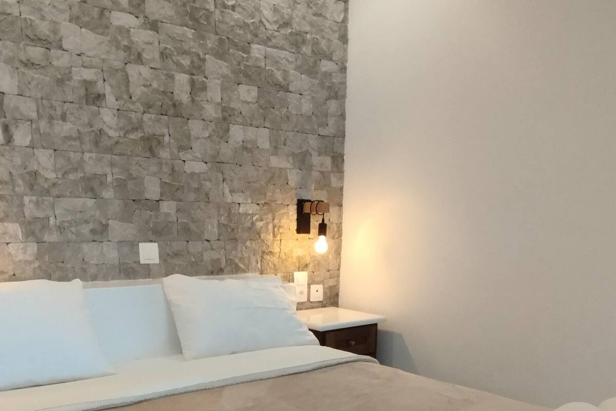 Ein Schlafzimmer mit Steinwand, einem Bett mit weißer Bettwäsche, einem Nachttisch mit Lampe und einem auf dem Bett liegenden zusammengeknüllten Handtuch.