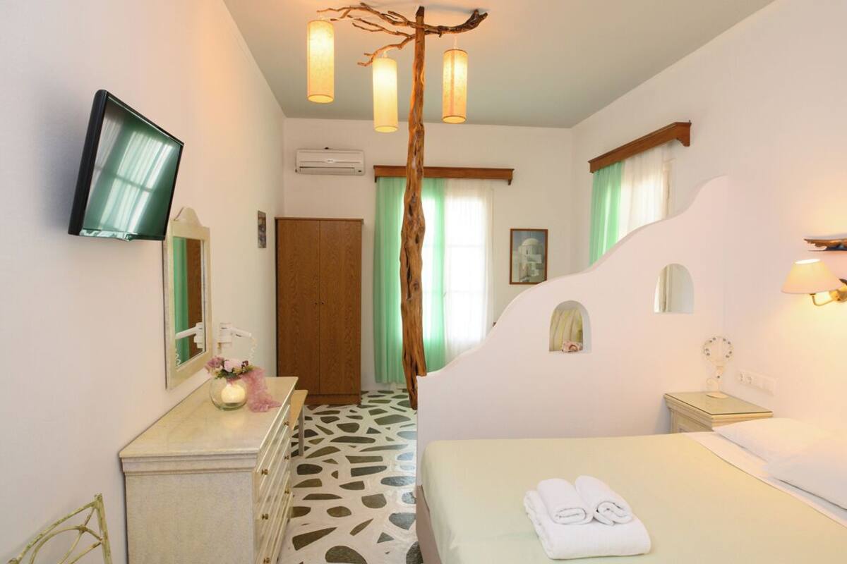 Ein Hotelzimmer mit Bett, Schminktisch, Spiegel, an der Wand montiertem Fernseher und einer auffälligen, baumförmigen Leuchte.