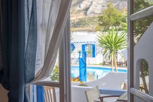 Quarto com vista para uma piscina, uma palmeira e uma paisagem montanhosa.