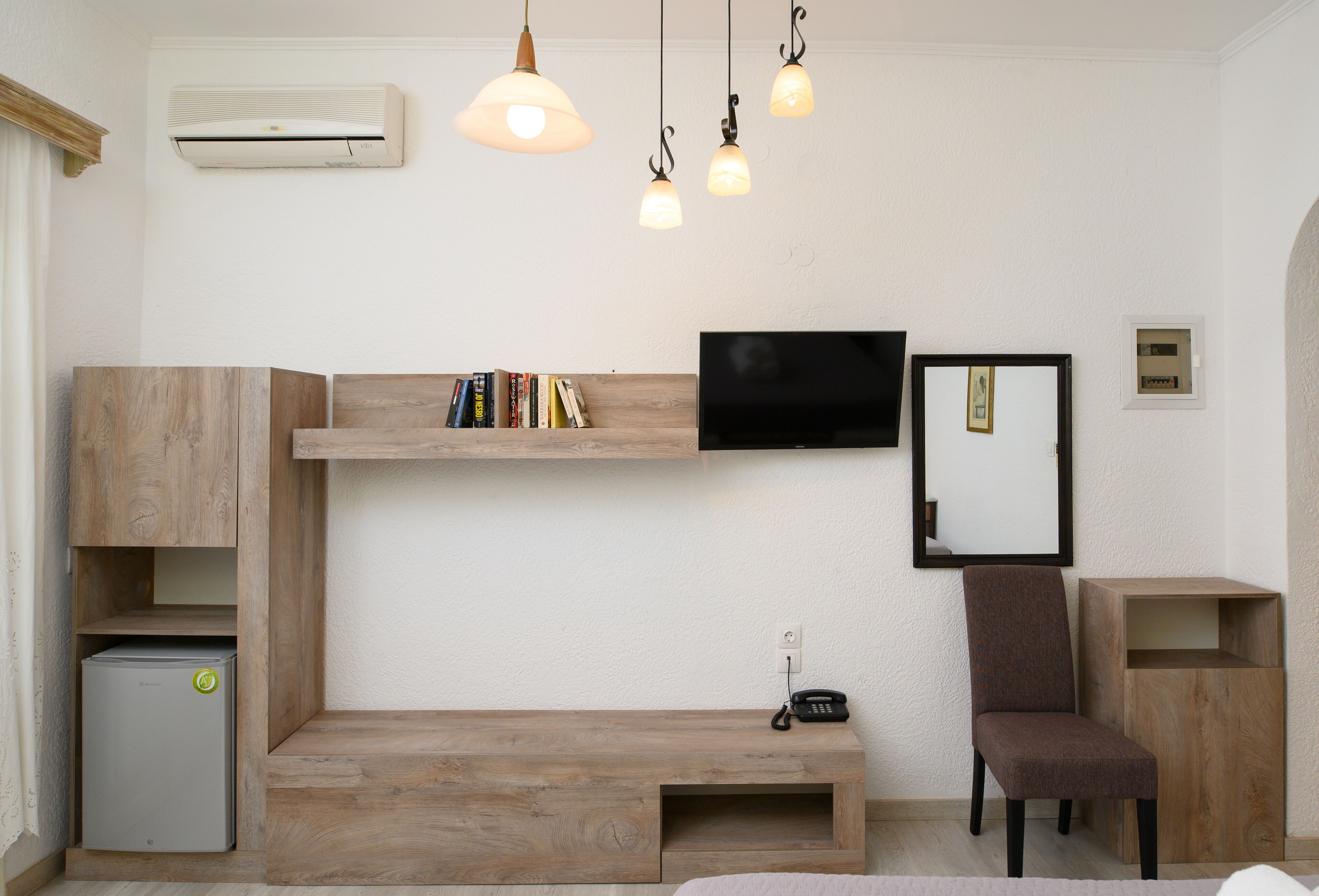 A modern room with a built-in bench, a small refrigerator, a TV mounted on the wall, and a wooden chair.
