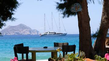 A table and chairs by the sea with a sailboat in the background.