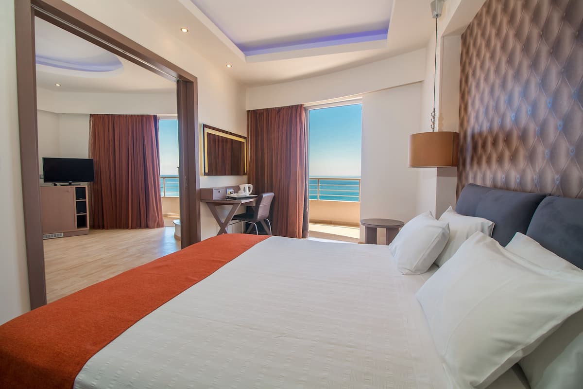 Une chambre d’hôtel avec un grand lit, un bureau, une télévision et une vue sur la mer.
