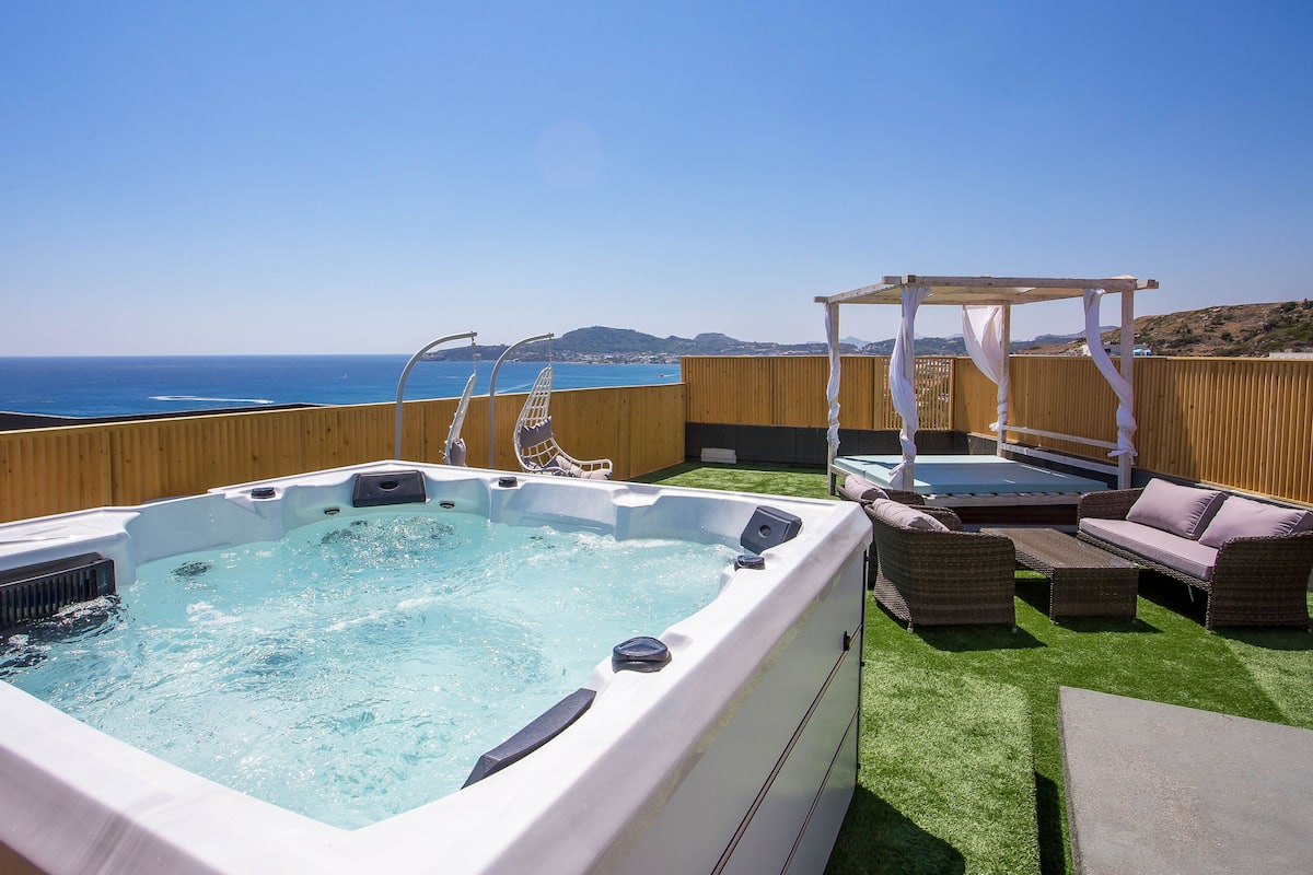 Un bain à remous doté d’une terrasse en bois et de mobilier d’extérieur, offrant une vue imprenable sur un océan d’un bleu profond.